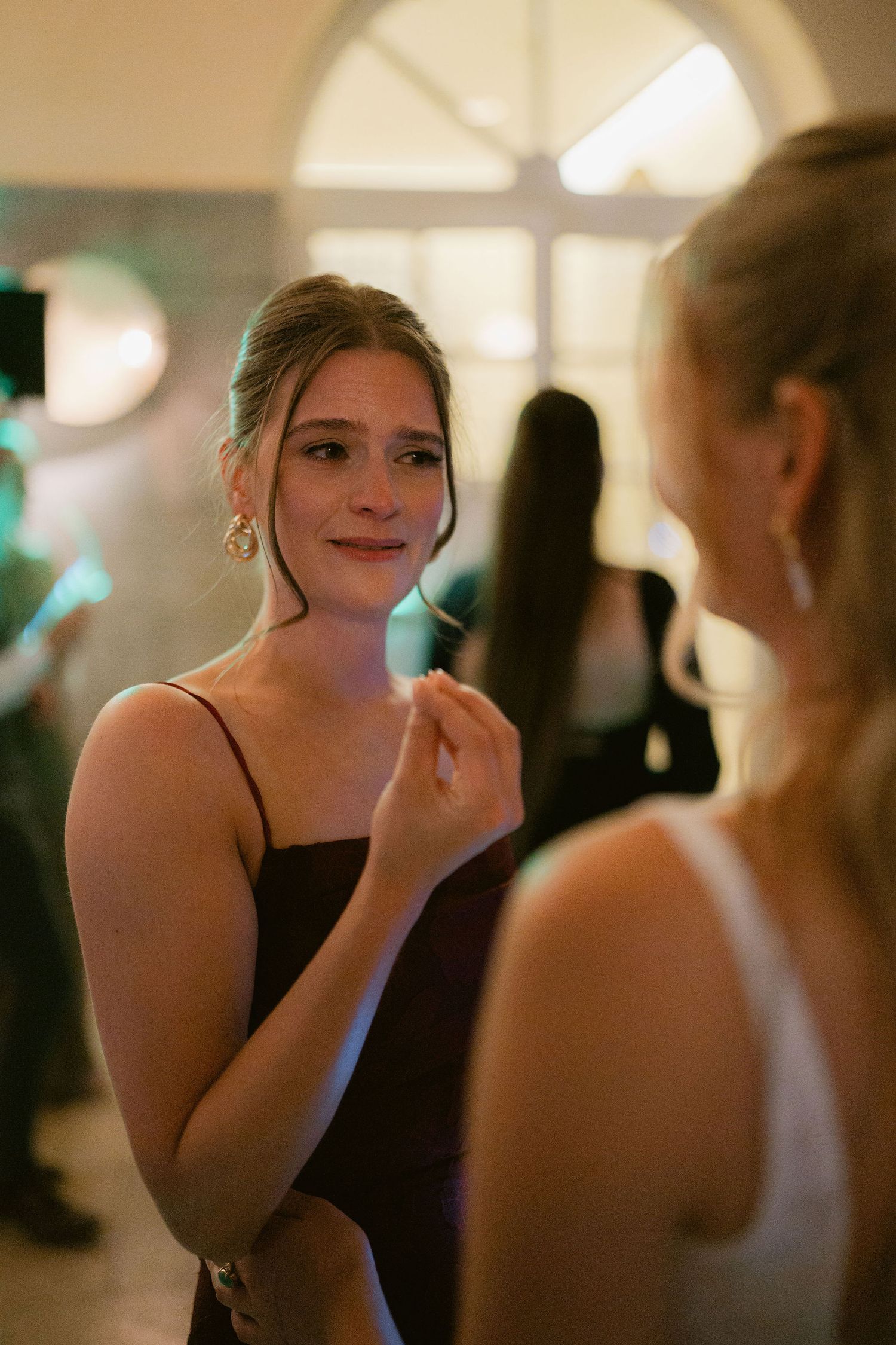 A bridesmaid in a dark dress smiles warmly while conversing at an elegant wedding reception.