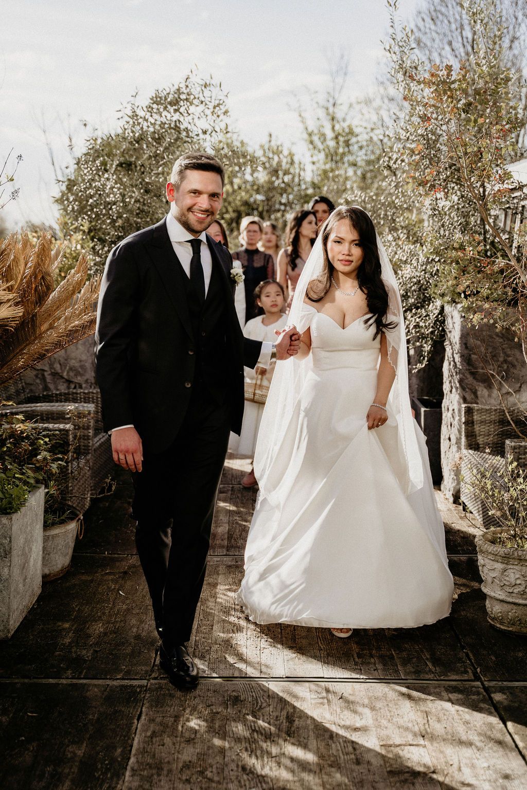 A bride and groom share romantic moments in a sunlit garden setting during their wedding photoshoot.