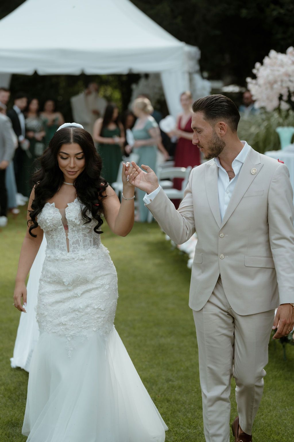 Newlywed couple shares joyful laughter while walking on green lawn at outdoor wedding celebration.