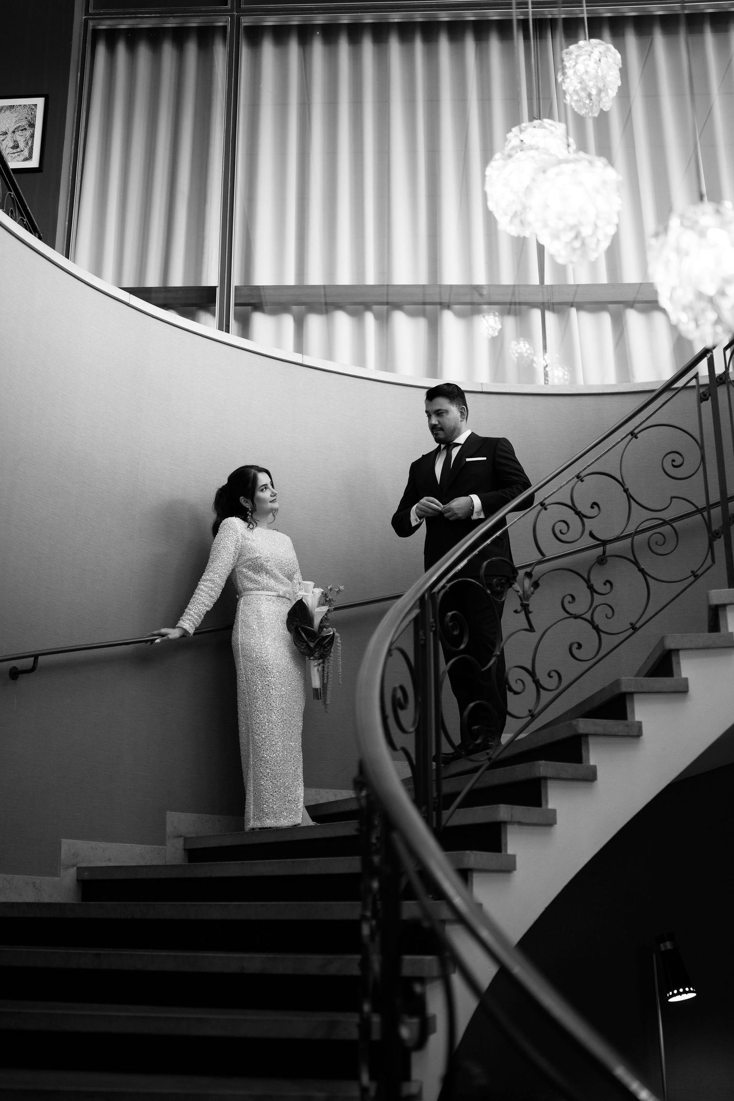 Elegant bride and groom on curved staircase in black and white wedding portrait.