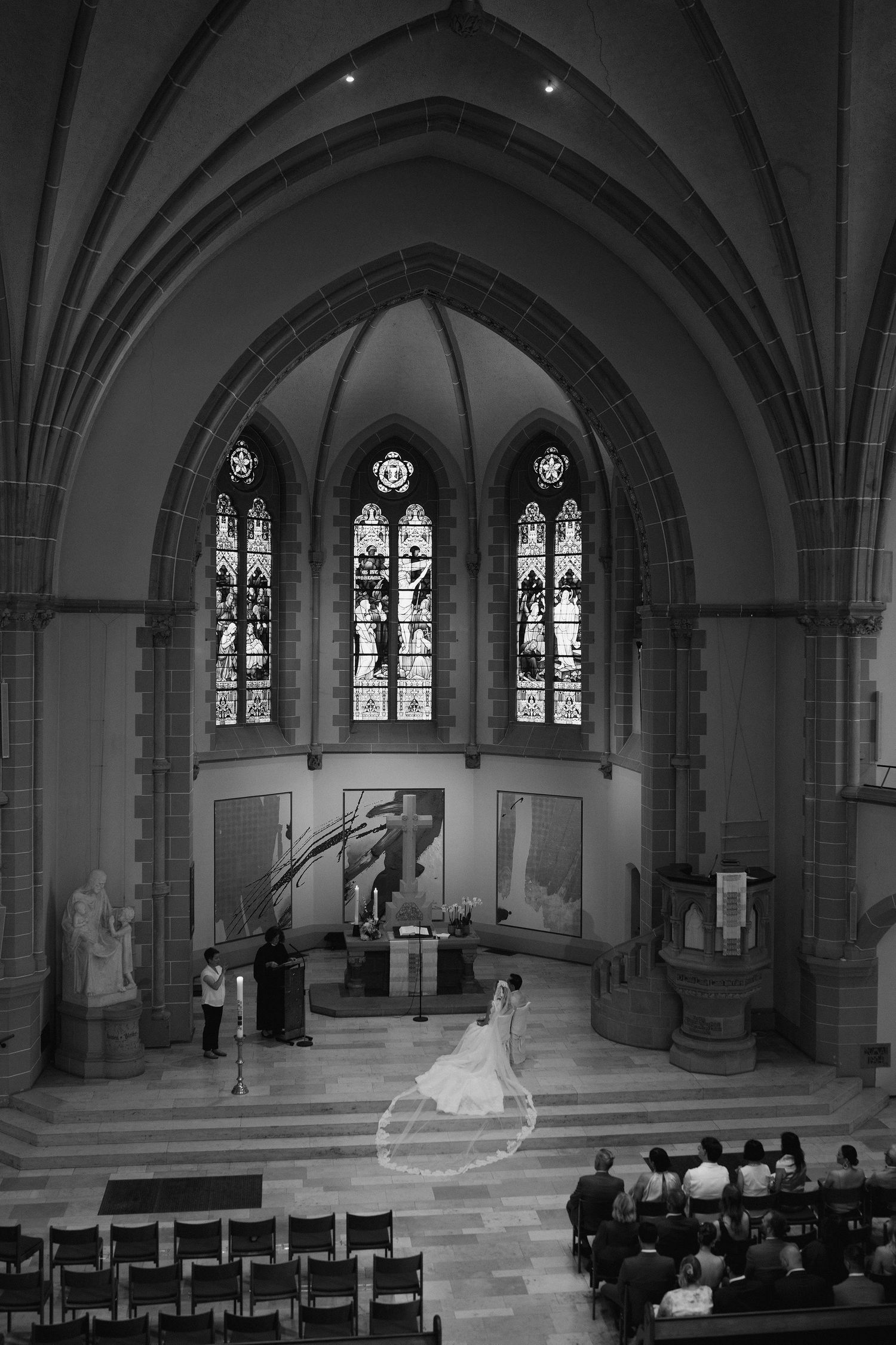 Black and white aerial view of bride at church altar beneath Gothic arched ceiling and stained glass.