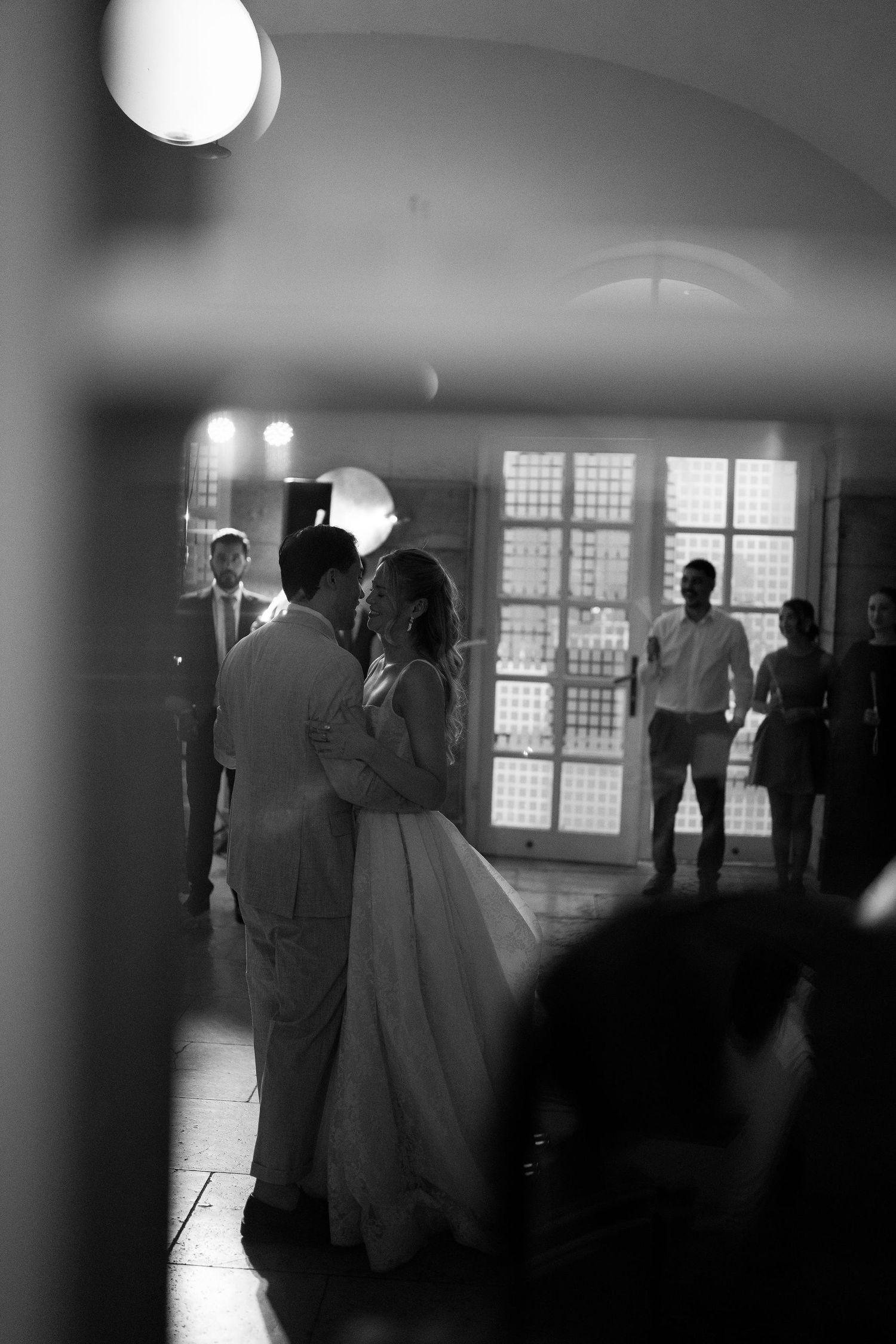 Black and white photo of bride and groom sharing first dance at wedding reception with guests watching.