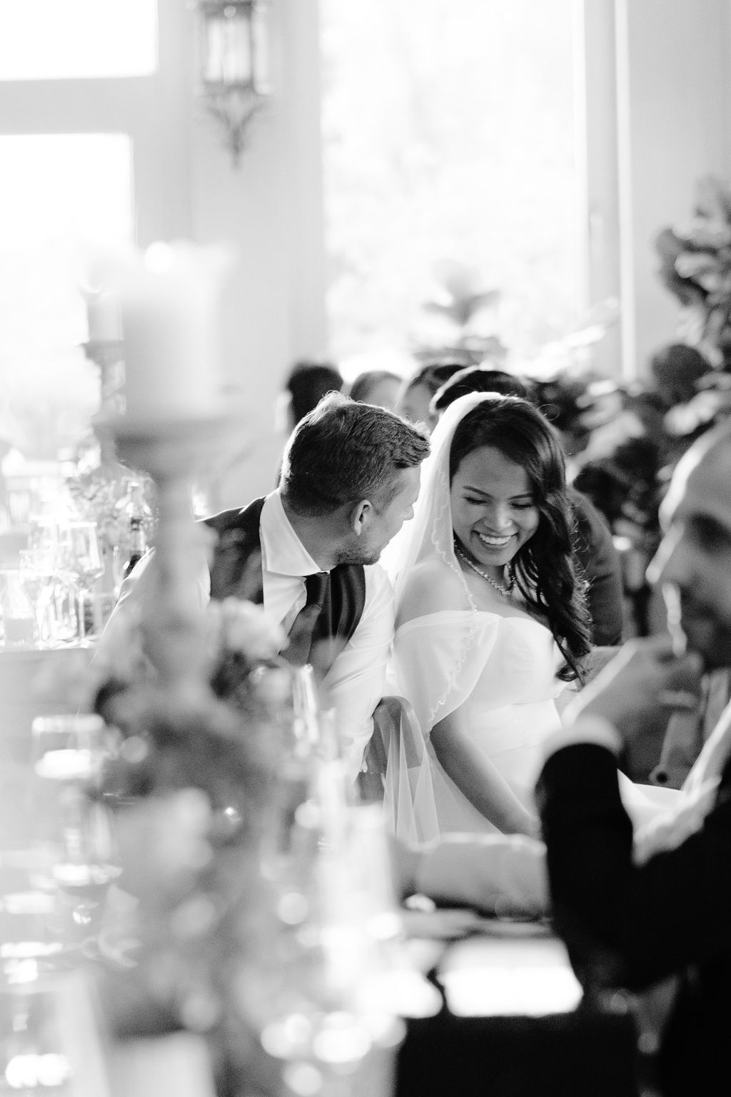 Black and white candid photograph of a joyful moment between a couple at a wedding reception table.