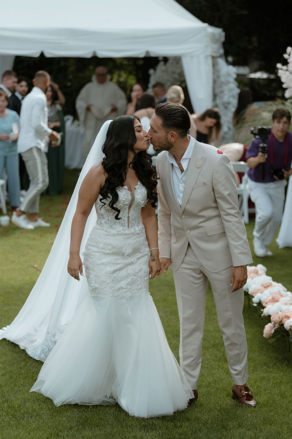 A newlywed couple walks together on a grassy lawn during their outdoor wedding captured in a series of photos.