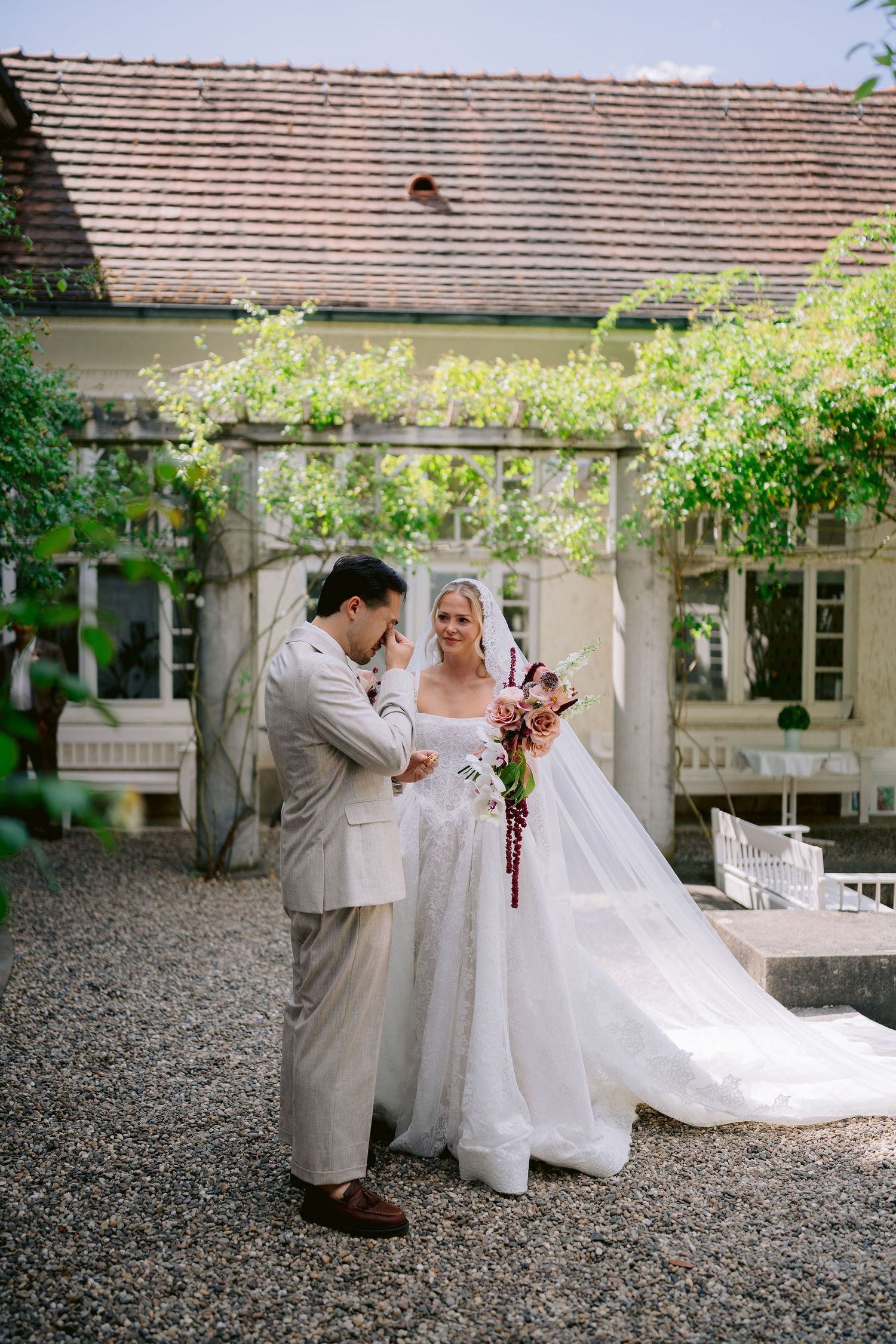 Bride in white ball gown and groom in beige suit share a tender first look moment in a charming garden courtyard.