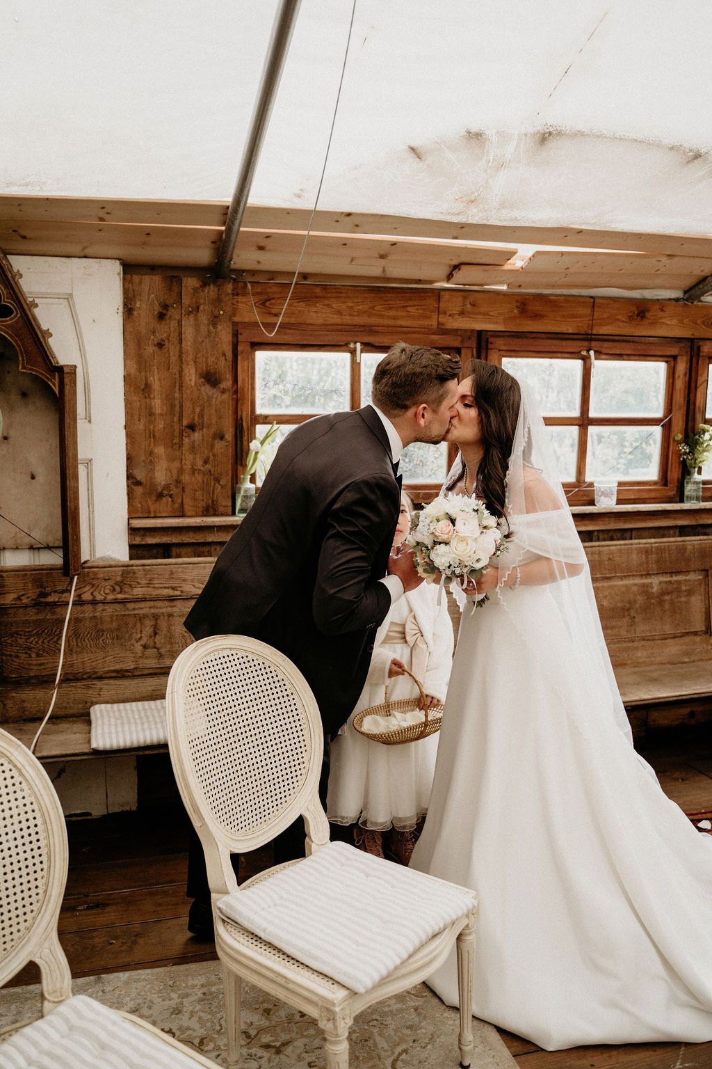 A romantic wedding moment captured across multiple angles as a couple shares a kiss in a rustic wooden venue.