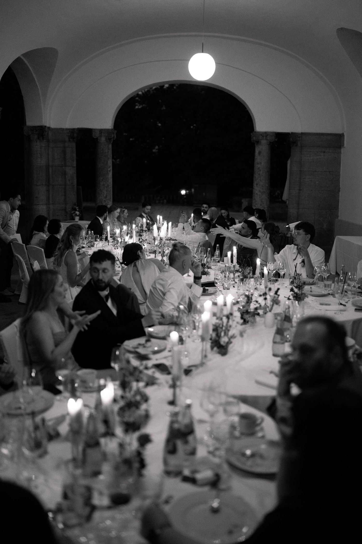 Elegant black and white wedding reception dinner with candlelit long tables under arched venue.