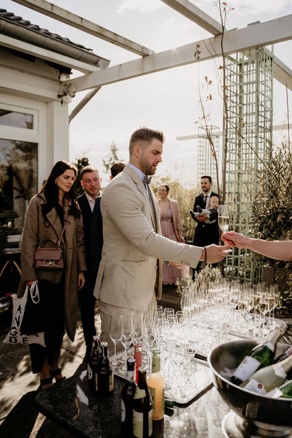 Guests gather around a wine tasting setup with multiple glasses in a bright sunlit conservatory space.