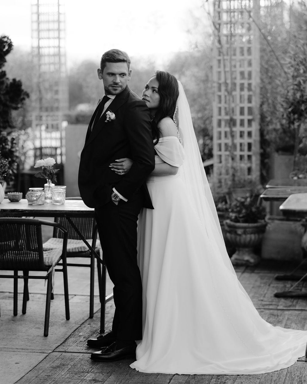 A newlywed couple shares an intimate moment on an outdoor patio in classic black and white photography.