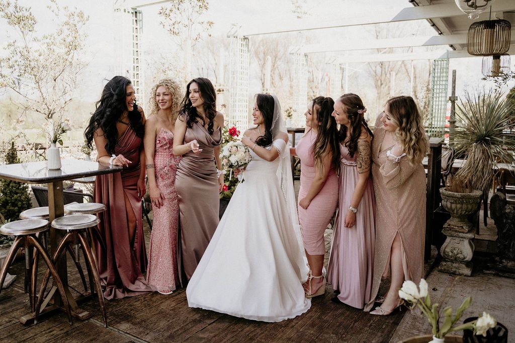 A wedding party in pink and mauve dresses gather together on a patio during a springtime celebration.