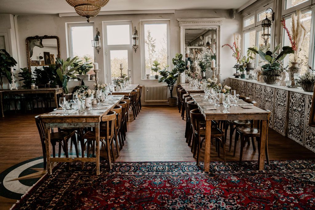 An elegant wedding reception table setting with white florals, rustic vineyard chairs and antique rug details in a bright room.