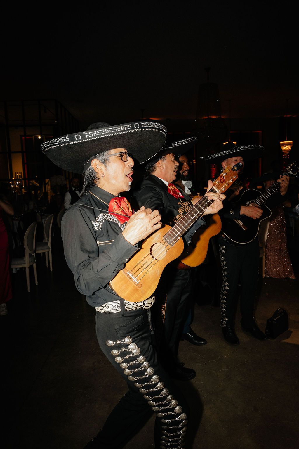 Mariachi musicians perform in traditional outfits with guitars during a nighttime event.