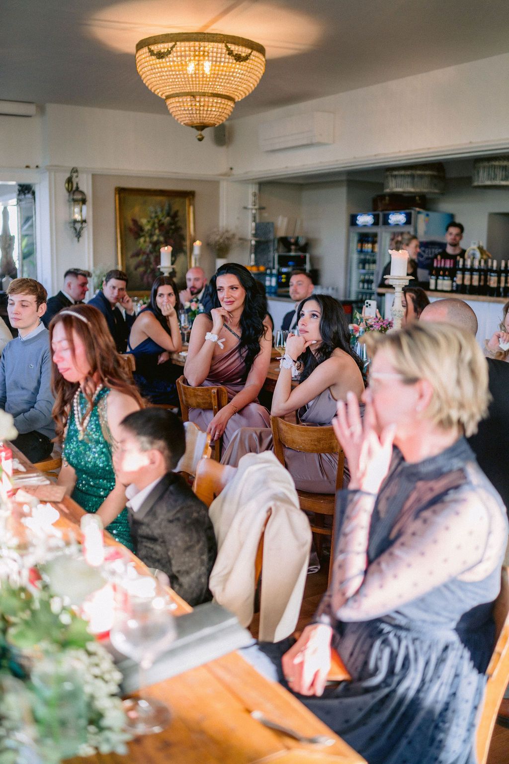 Wedding guests enjoying a celebration at a reception venue with an elegant chandelier overhead.