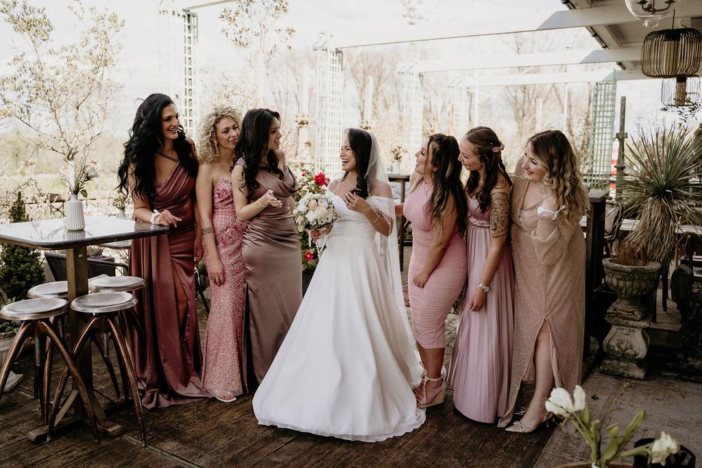 A group wearing blush pink bridesmaid dresses gathers for candid moments during an outdoor wedding celebration.