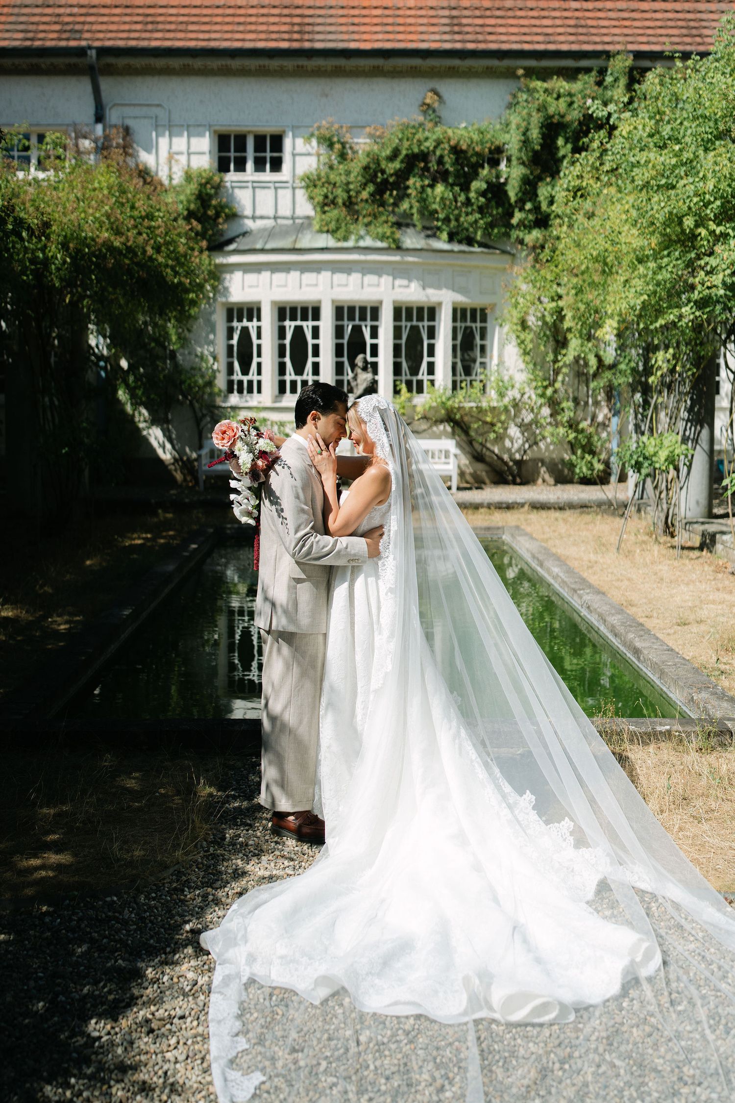 Bride and groom share a romantic kiss beside a reflecting pool at an elegant garden wedding venue.