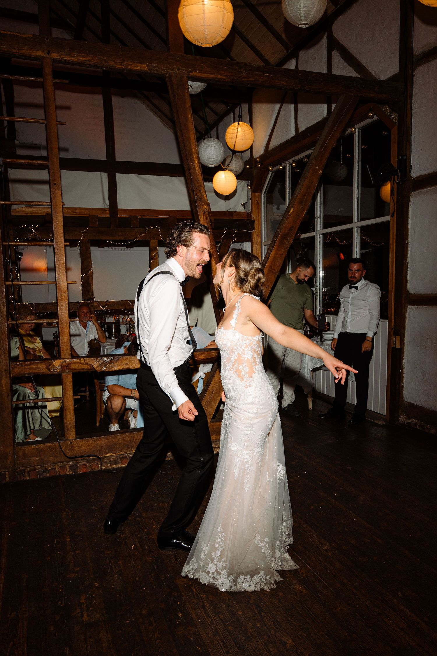 Bride and groom share their first dance in a rustic barn venue adorned with hanging paper lanterns at their wedding reception.
