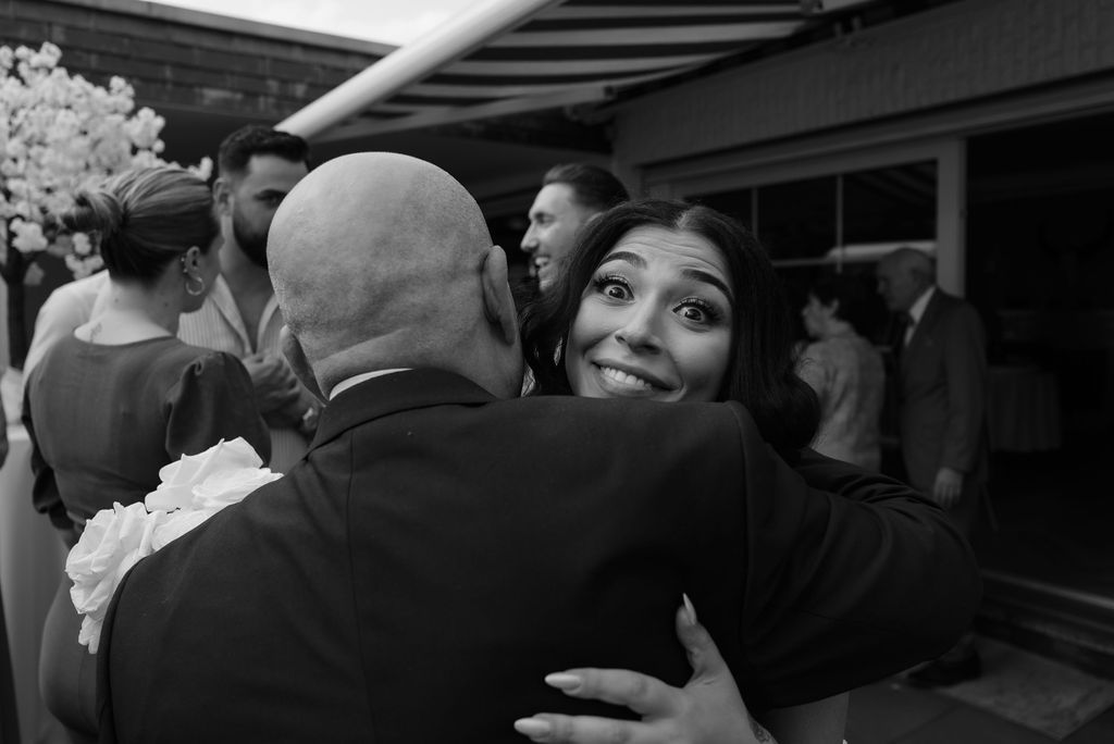 A heartfelt embrace is shared between two people at a social gathering, captured in black and white photography.