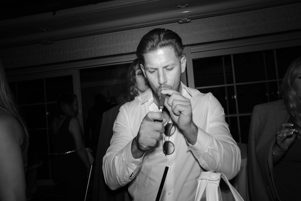 A person in light colored clothing lighting a cigar in dim lighting.