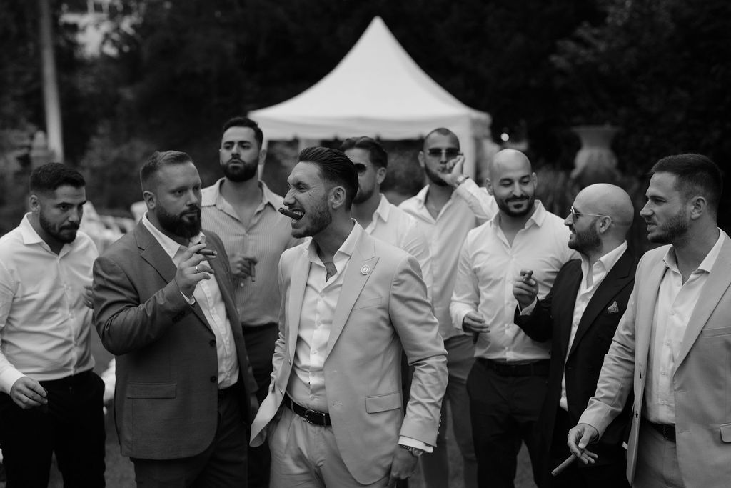 A group of well-dressed guests gathered outdoors under a white tent for a celebration.