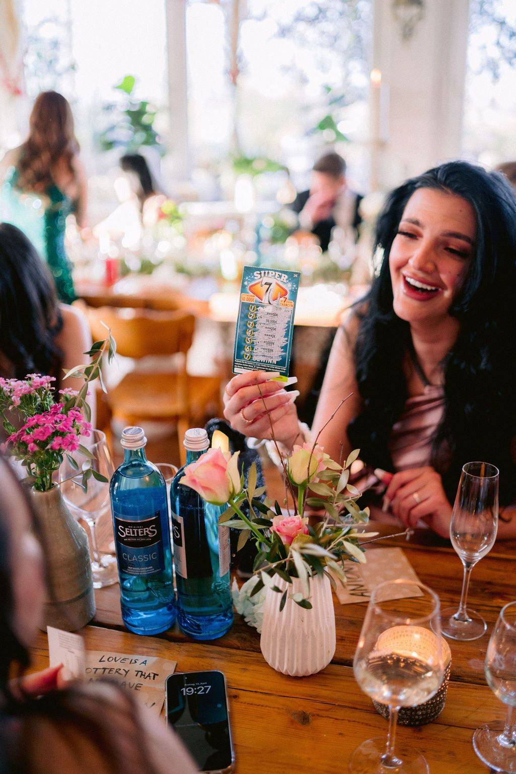 Wooden table set with blue bottles, wine glasses and pink flowers for a celebratory gathering.