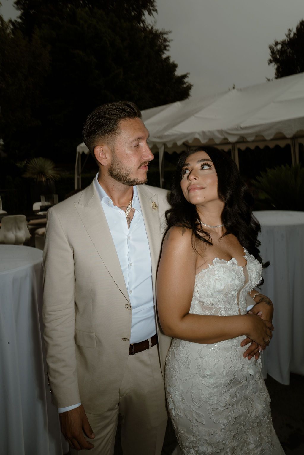 A couple shares an intimate moment at their outdoor wedding reception with white tents and tables in the background.