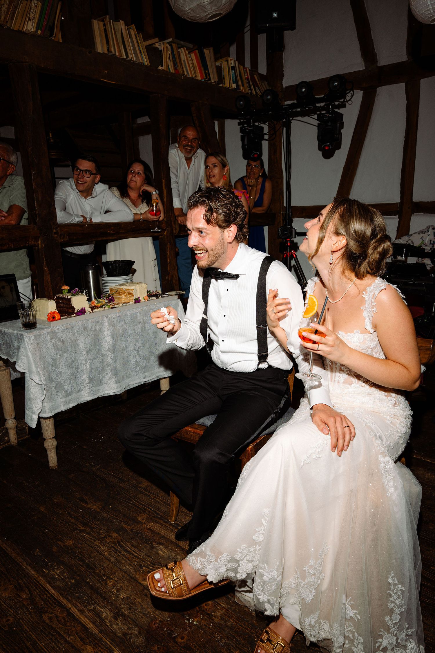 Bride and groom laughing together at wedding reception, holding champagne glasses in rustic barn venue.