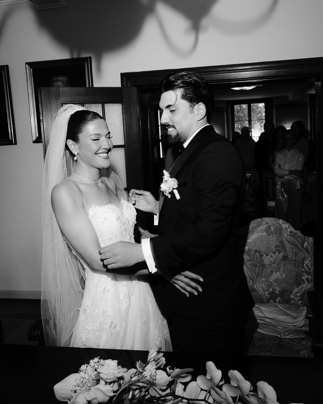 Black and white wedding photo of smiling bride and groom exchanging rings at the altar.