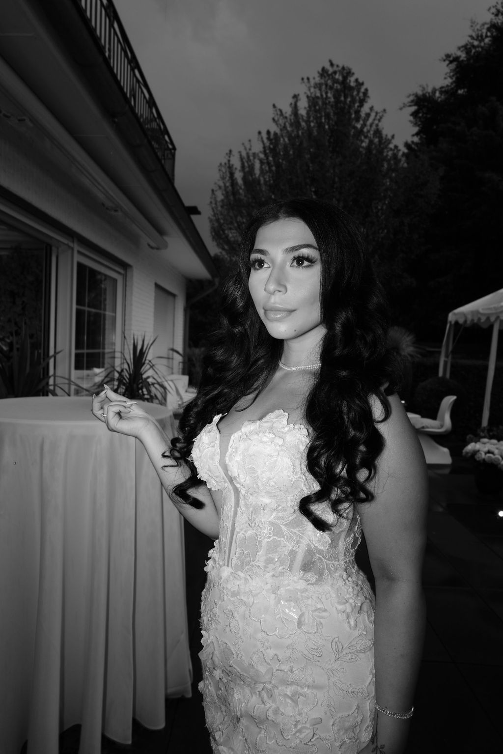 A black and white portrait of someone wearing an elegant lace wedding dress with long dark curls.