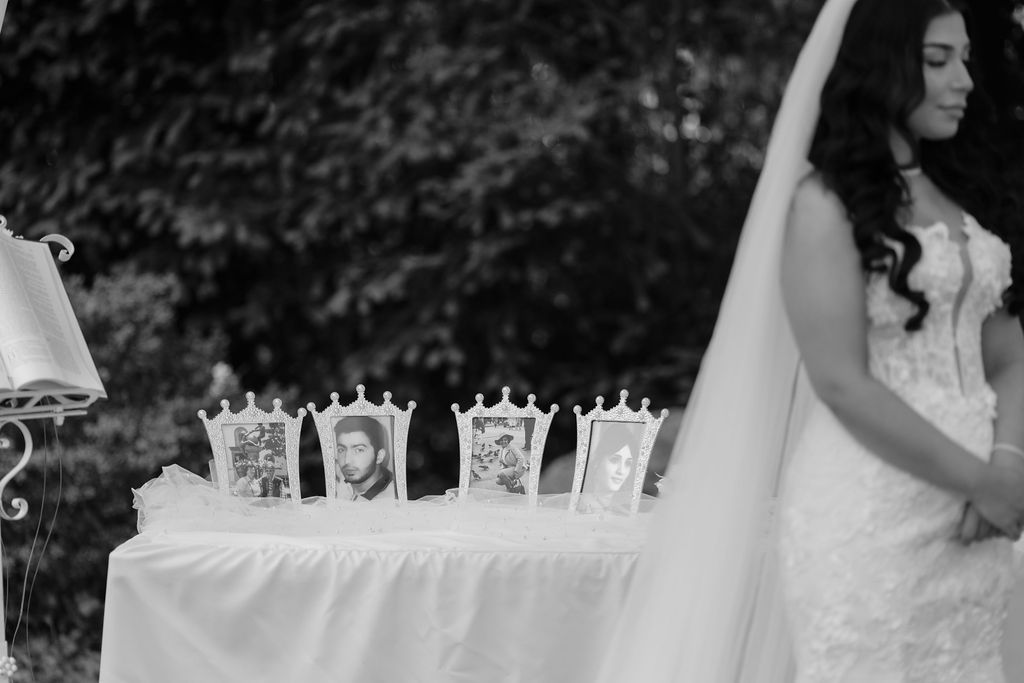 Black and white wedding photo showing decorative crown place settings on table beside flowing white bridal gown.