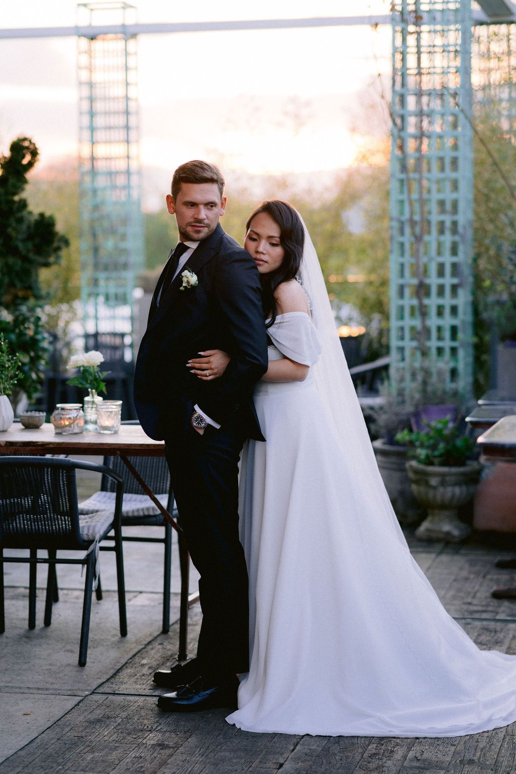 A bride and groom share intimate moments on an outdoor patio with elegant trellis decor at sunset.