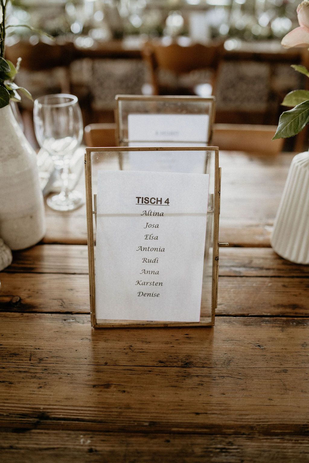 Elegant table seating chart in gold frame displays guest names for table 4 at rustic wedding reception.