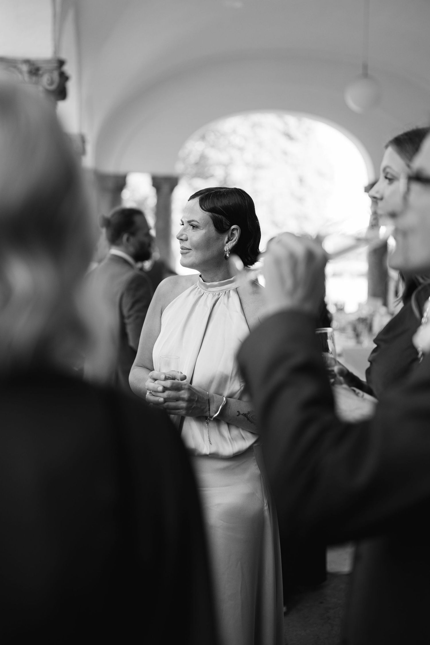 Black and white photo of an elegant woman in a halter gown mingling with guests at a formal wedding reception.