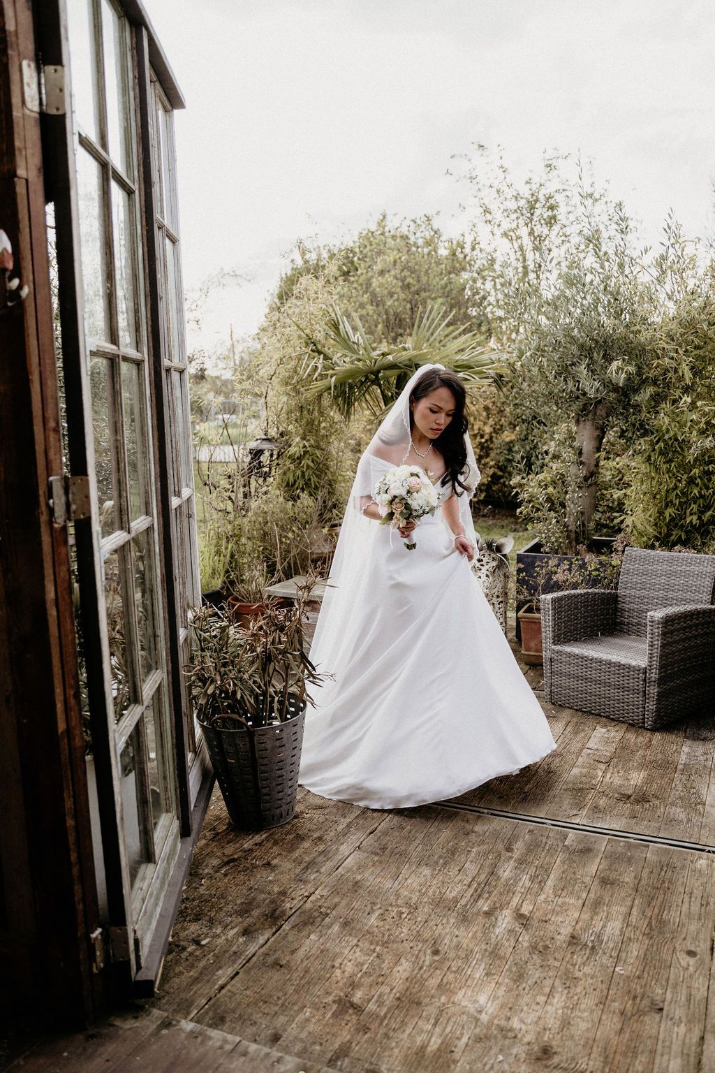 A beautiful bride spins and twirls in a flowing white wedding dress on a rustic wooden deck surrounded by greenery.