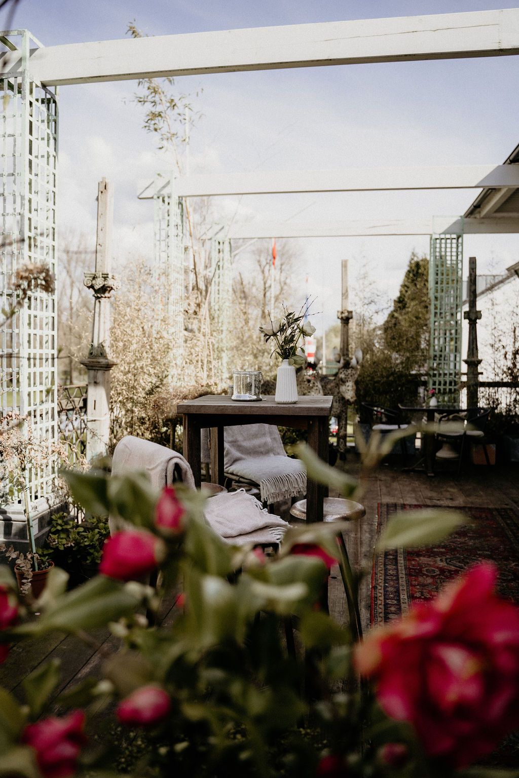 White outdoor pergola decorated with twinkle lights and red flowers in a garden reception setting at dusk.