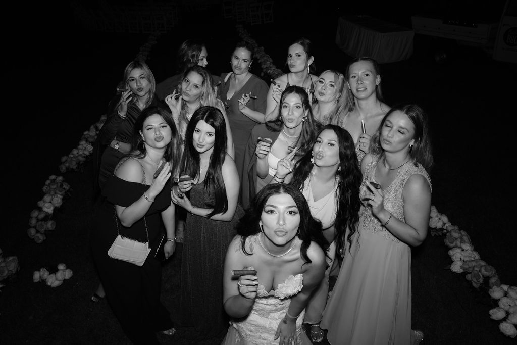 Group of wedding reception guests dancing and celebrating together in a dark venue with festive lighting.