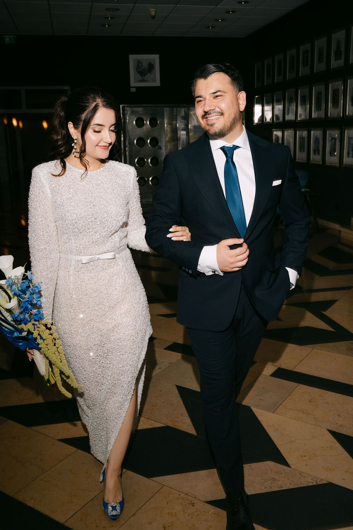 Elegant bride and groom walking arm in arm through decorated venue on wedding day.