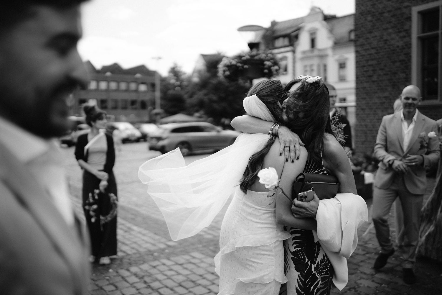 Bride embraces a guest in an emotional hug outside after a wedding ceremony in black and white.