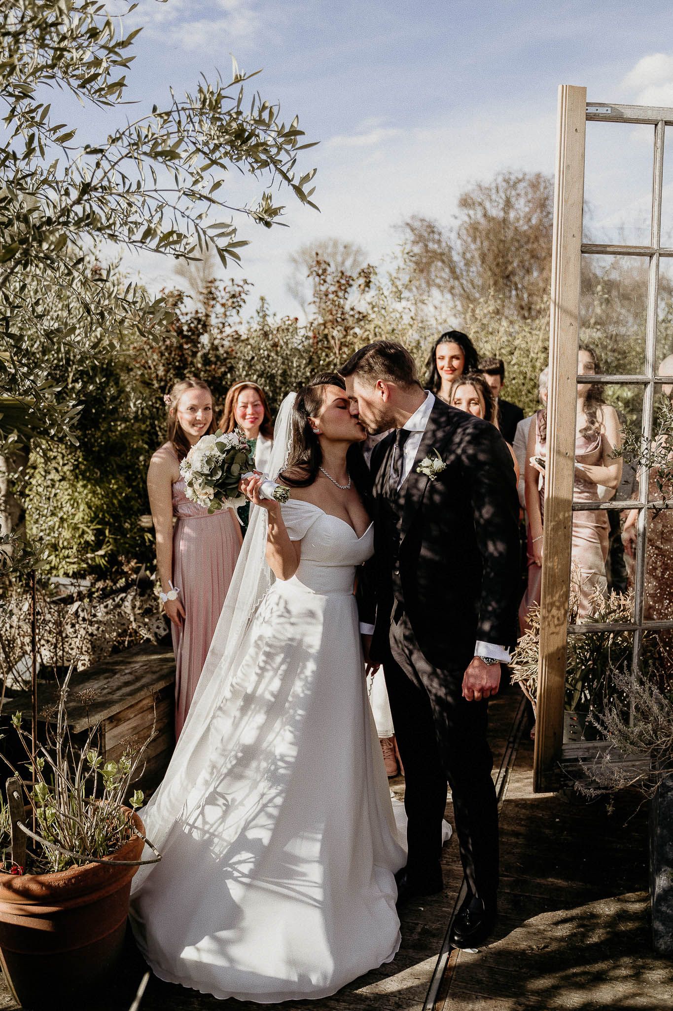 Wedding party laughs together during outdoor ceremony with rustic wooden backdrop and desert landscaping in natural light.