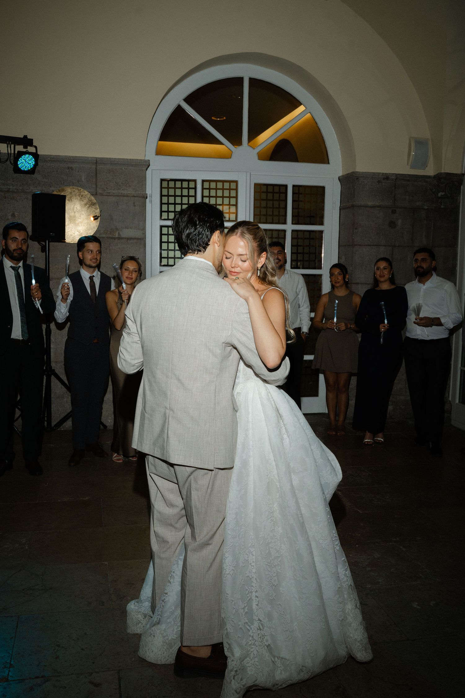 Bride and groom share their first dance at wedding reception while guests watch and applaud in elegant venue.