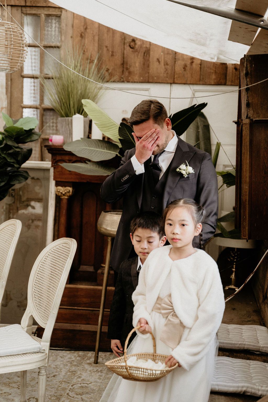 Four young boys in white dress shirts sit at a reception or event with white plastic chairs in the background.
