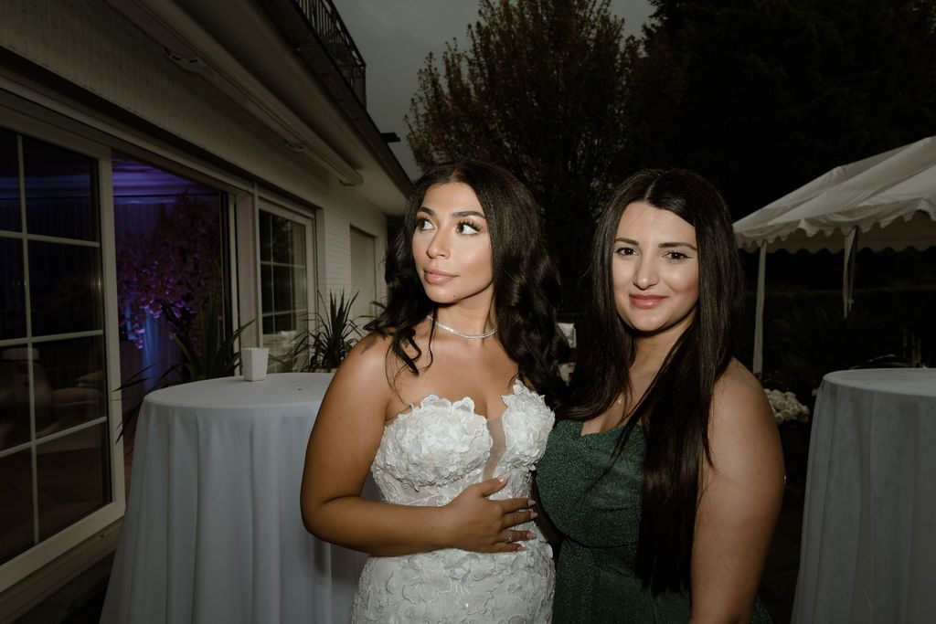 Two people in evening attire pose together at an outdoor event with tent and lighting visible.