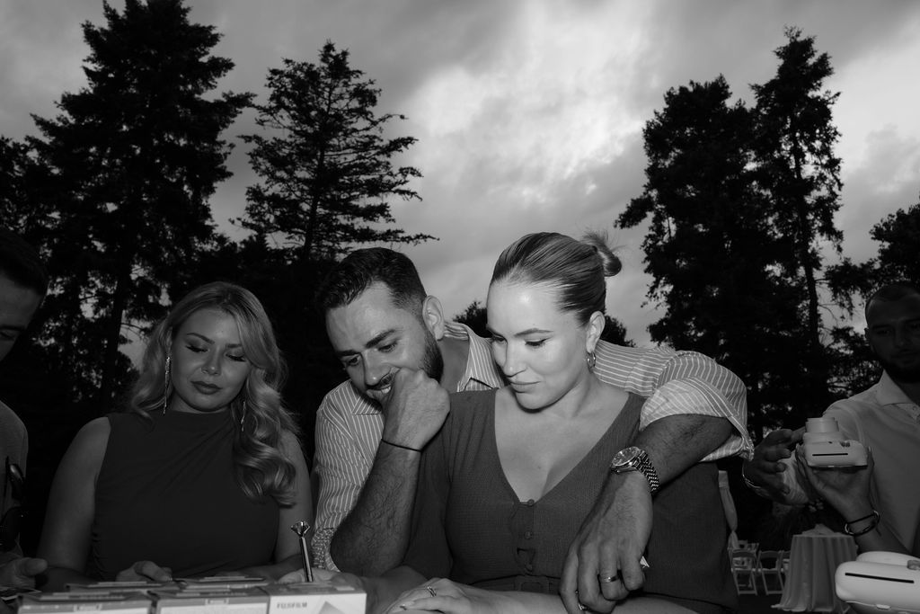A black and white candid photo of people gathered around a table at an outdoor event.