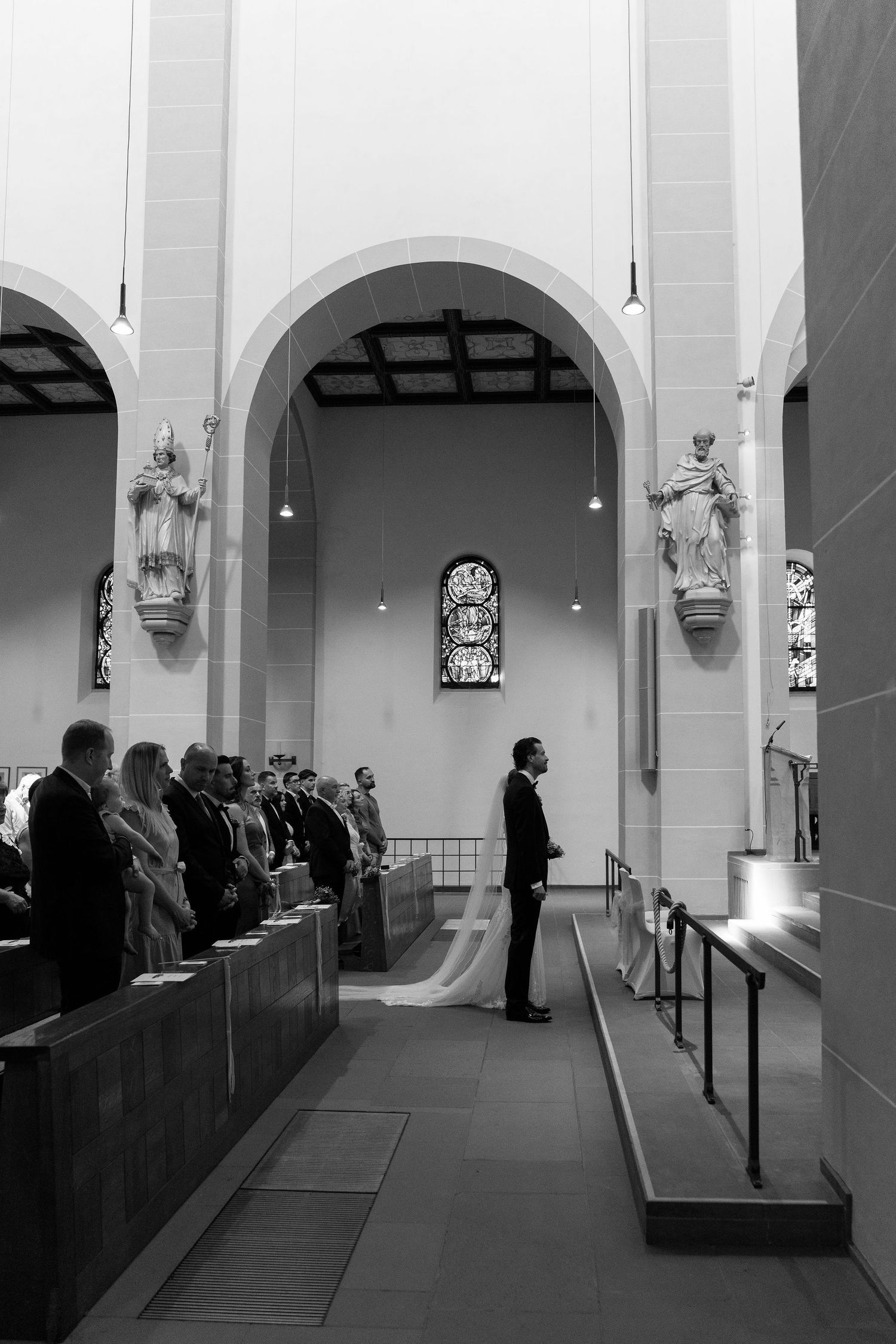 Black and white photo of a groom standing at the altar during a church wedding ceremony with guests seated in pews.