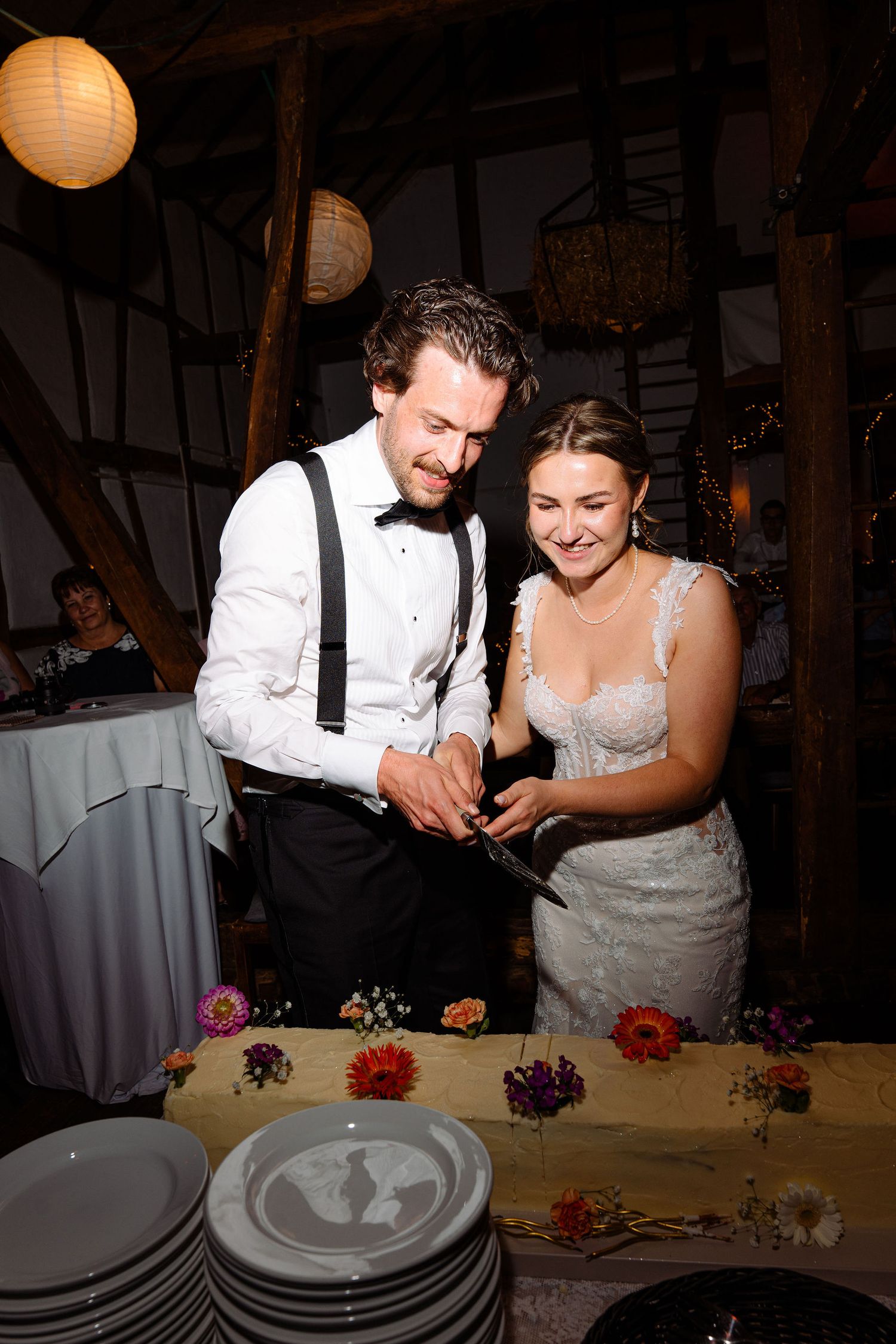 Bride and groom smiling while cutting their wedding cake together at a rustic barn reception venue.