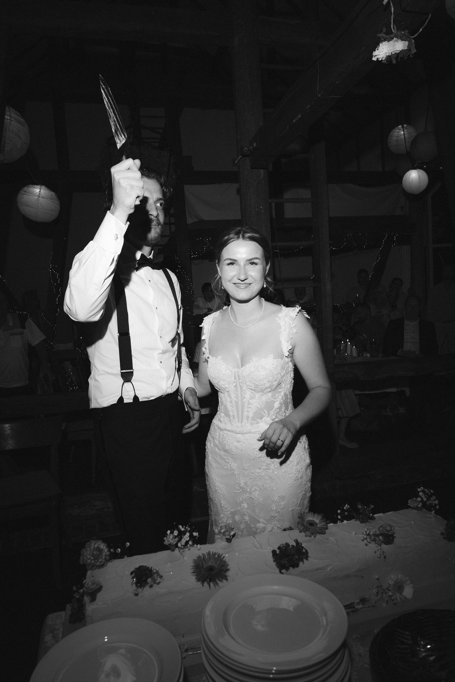 Black and white photo of a bride and groom cutting their wedding cake at a reception.