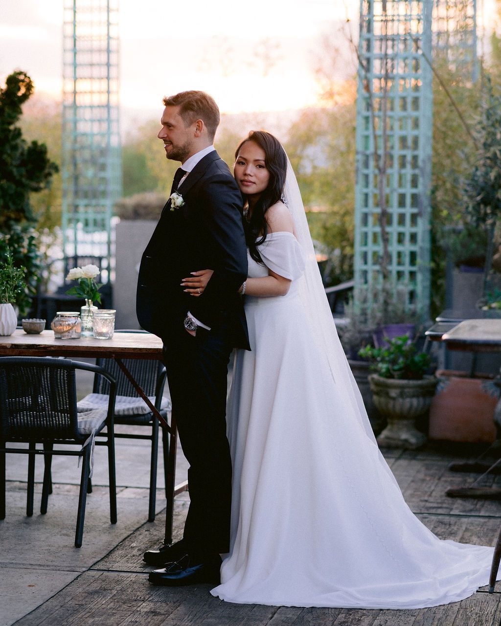 Wedding couple shares an intimate moment on an outdoor patio with elegant white trellis and garden decor at sunset.