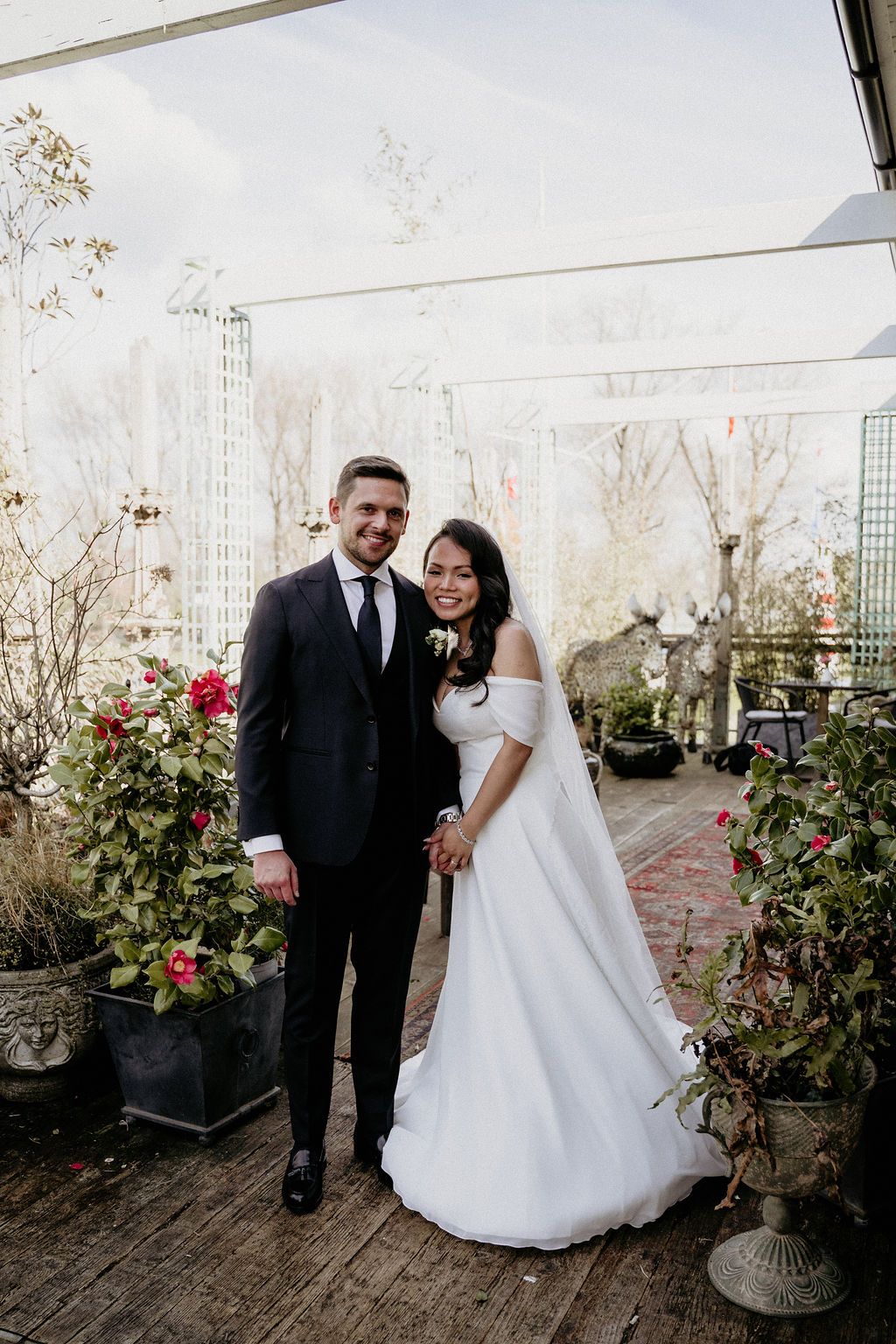 Couple shares romantic moments during outdoor photography session on a patio decorated with red roses and potted plants.