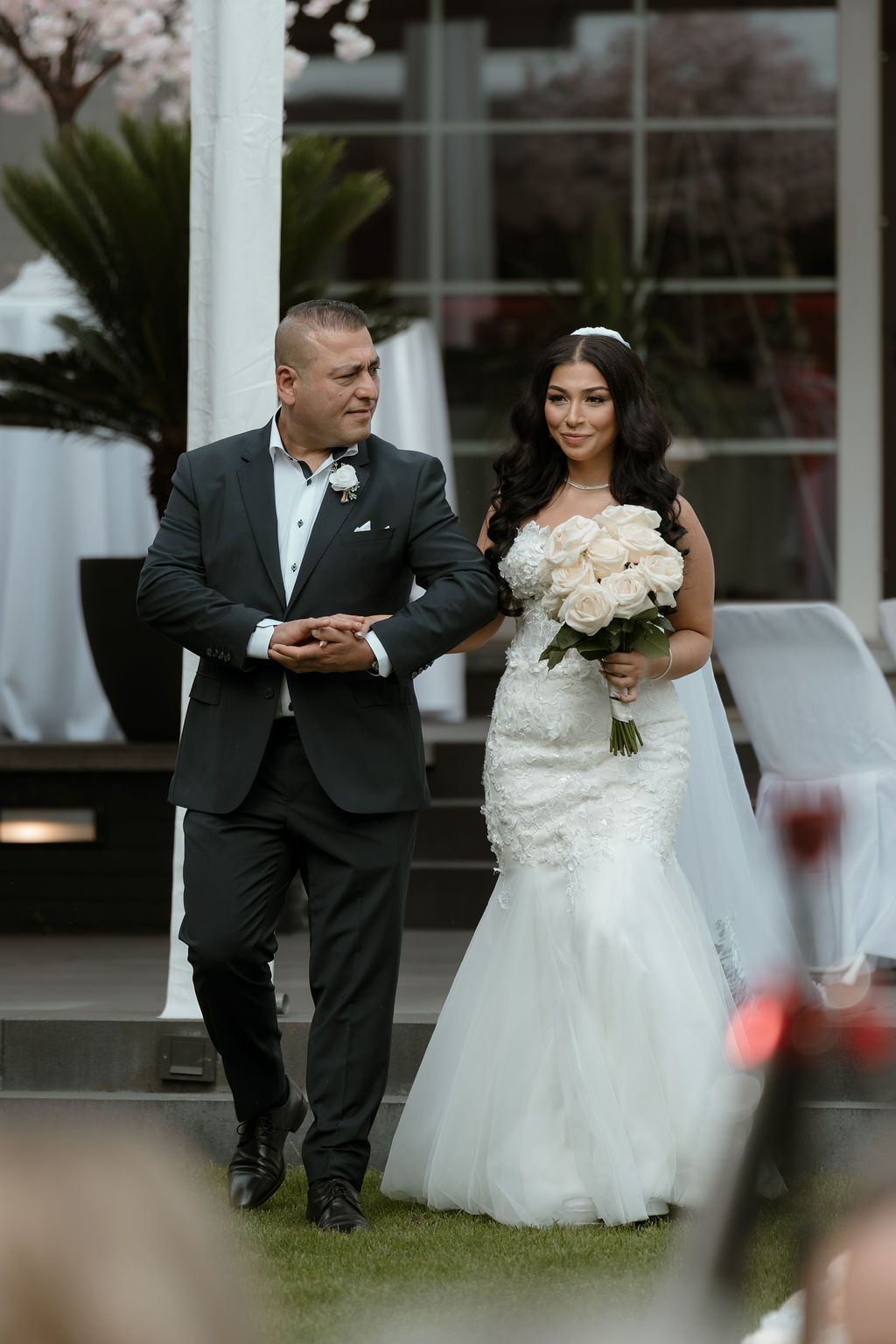 Couple in traditional wedding attire walking together on lush grounds during an outdoor wedding celebration.