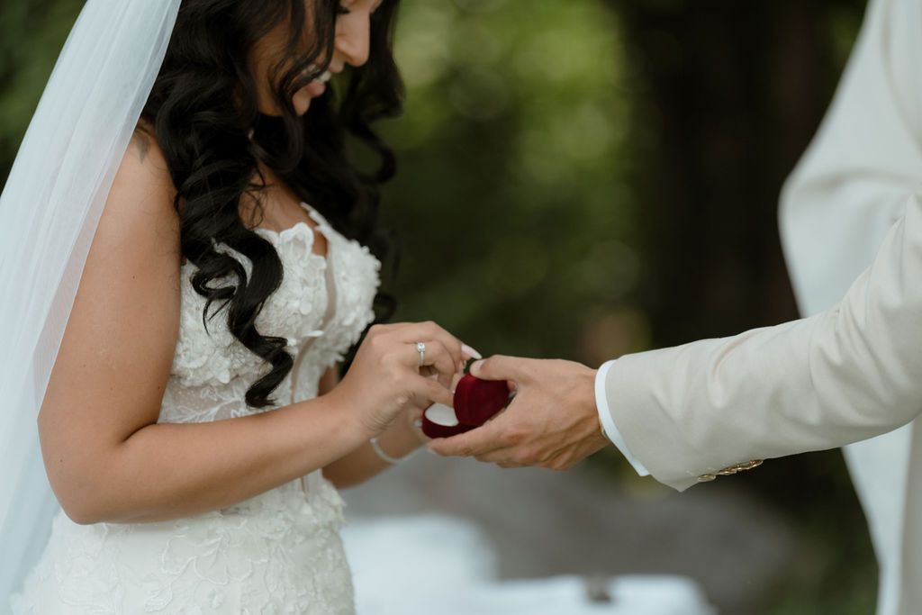 Wedding couple stands in formal garden exchanging rings during outdoor ceremony.