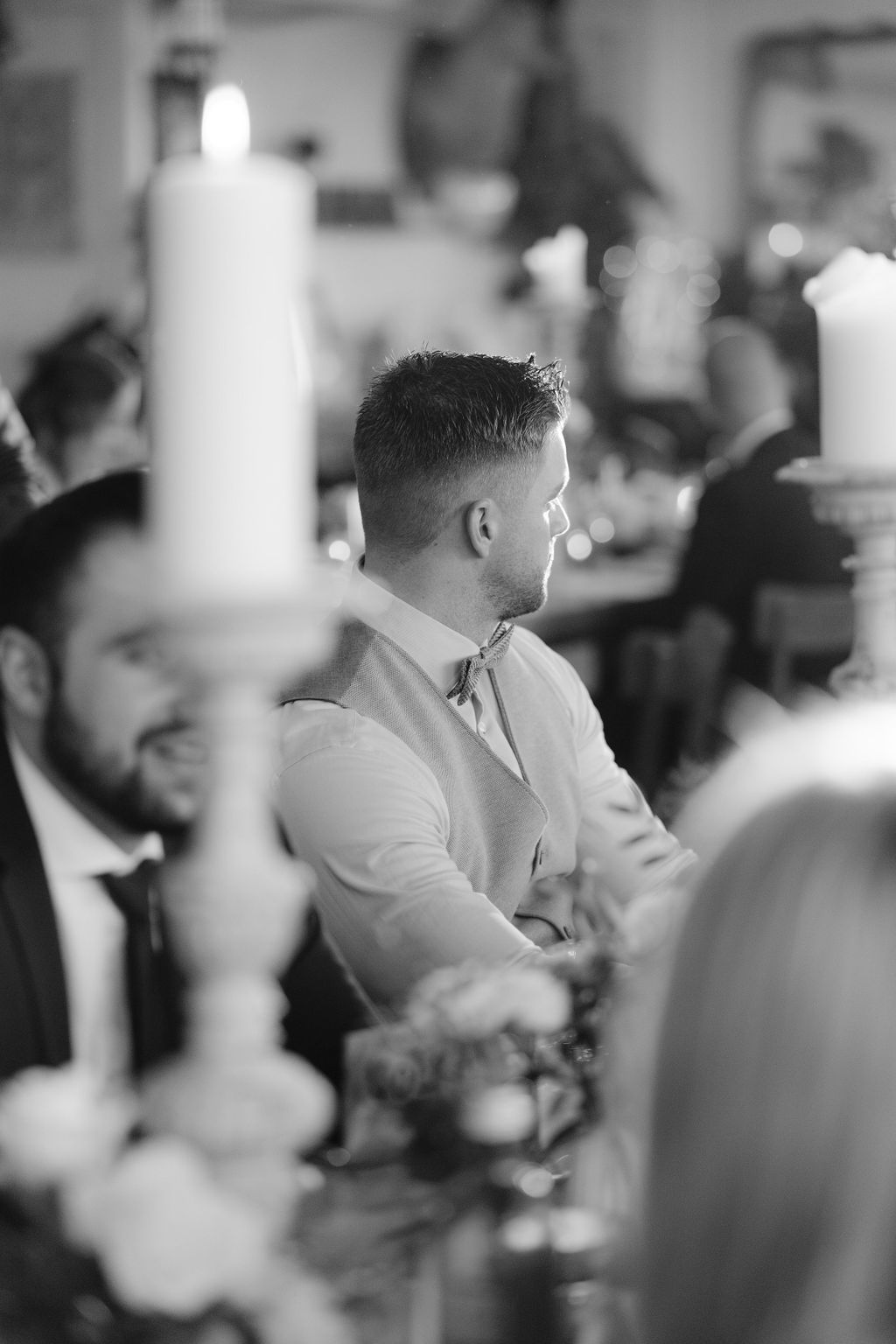 Black and white photo of a formal dinner reception with tall white candles in the foreground and guests seated at tables.
